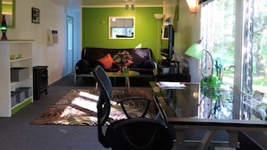 Un salon moderne avec un mur d’accent vert, un canapé noir, une table basse en verre et une vue sur l’extérieur grâce à de grandes fenêtres.