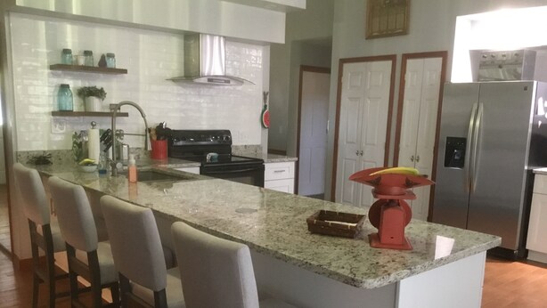 A kitchen with a central island, bar stools, a stainless steel refrigerator, and a stove.