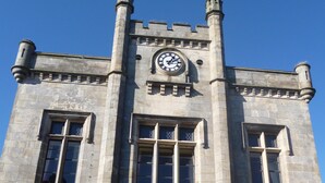 Un bâtiment historique en pierre, doté d’une tour horlogée, de grandes fenêtres et d’une clôture en métal.