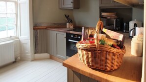 Une cuisine avec des meubles blancs, un four à micro-ondes, une bouilloire et un panier d’épicerie sur le plan de travail.
