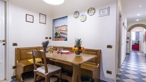 A dining area with a wooden table, benches, and a fruit bowl. There are framed pictures on the wall and a painting above the table. - Beautiful apartment sleeps  in the city centre of Florence (Firenze)