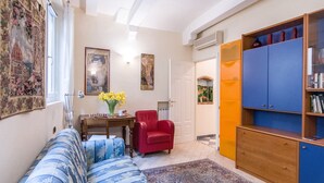 A living room with a sofa, a red chair, a wooden cabinet, and a chess table. - Beautiful apartment sleeps  in the city centre of Florence (Firenze)
