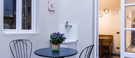 A small patio with a round table and two chairs, a potted plant, and a window.