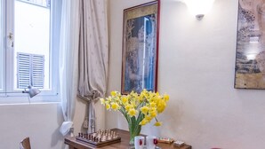 A room with a wooden table, a chessboard, a vase with flowers, a red chair, and a window with curtains. - Beautiful apartment sleeps  in the city centre of Florence (Firenze)