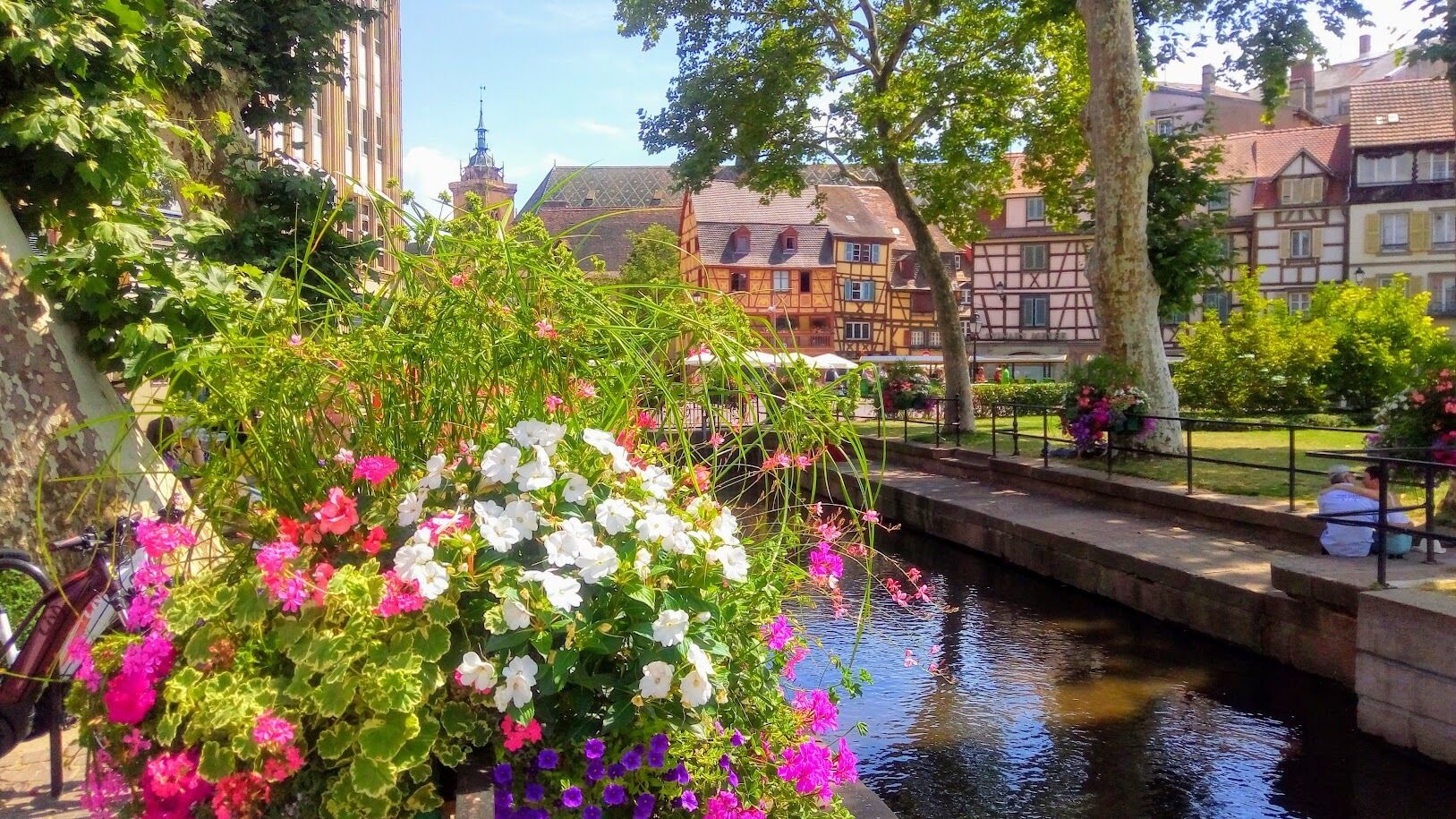 A canal with a bridge, surrounded by colorful flowers and traditional European buildings.