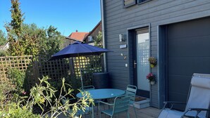 Un patio con una mesa, sillas, una sombrilla azul y una terraza de madera.