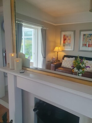 A room with a fireplace, a mirror reflecting a bed with a floral arrangement, and a window with curtains. - A Little Gem in The West Highlands, Argyll Inveraray Loch Fyne views, sleeps 4 (Inveraray)