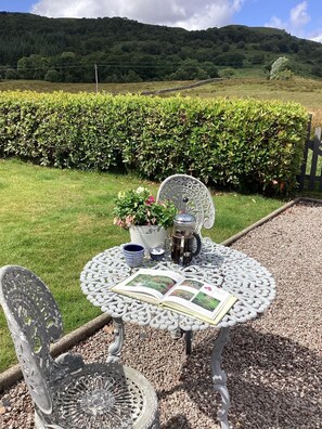 An outdoor seating area with a round table and chairs, a book, a teapot, and a cup.