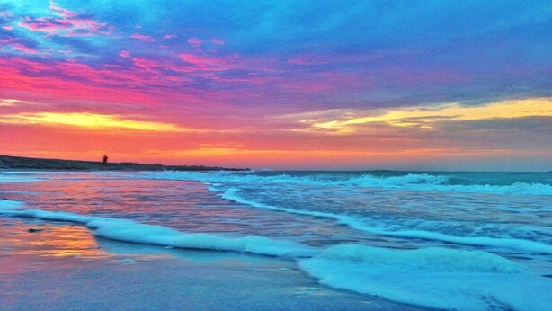 Una playa con olas y un atardecer.