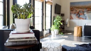 A living room with a potted plant, a stack of books, and a painting on the wall.