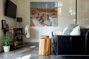 Un salon moderne avec un canapé en cuir noir, une table basse en bois, une plante en pot, un tableau accroché au mur et un téléviseur à écran plat.