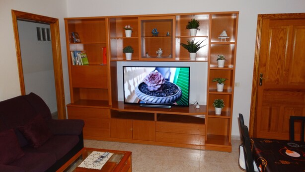 A living room with a wooden entertainment unit, television, and various decorative items.