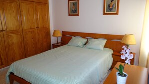 A neatly made bed with patterned bedding, two bedside lamps, a nightstand with a potted orchid, and wooden wardrobe doors.