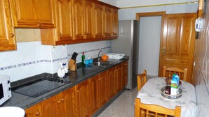 A kitchen with wooden cabinets, a stainless steel refrigerator, a sink, and a dining table with chairs.