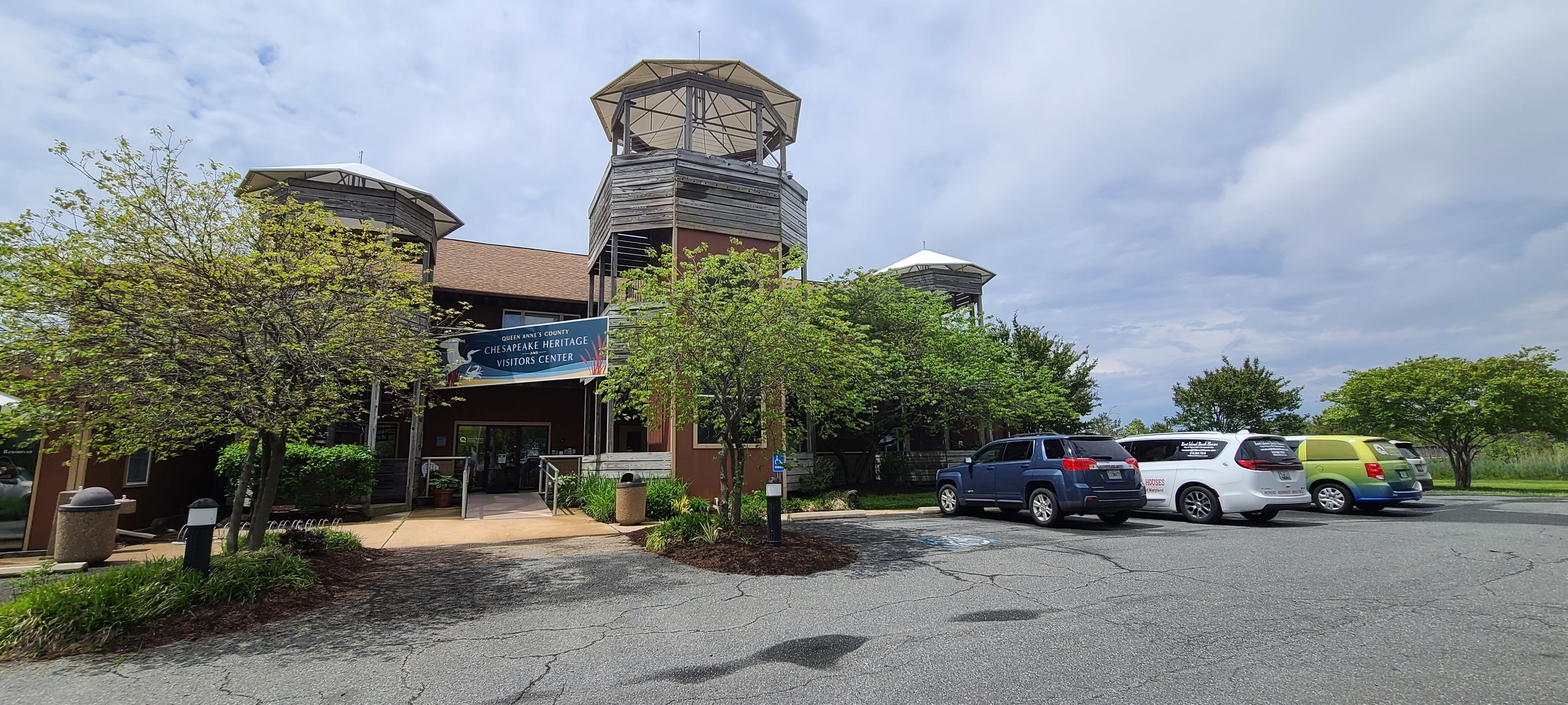 A building with a clock tower, a visitors center sign, and parked cars.