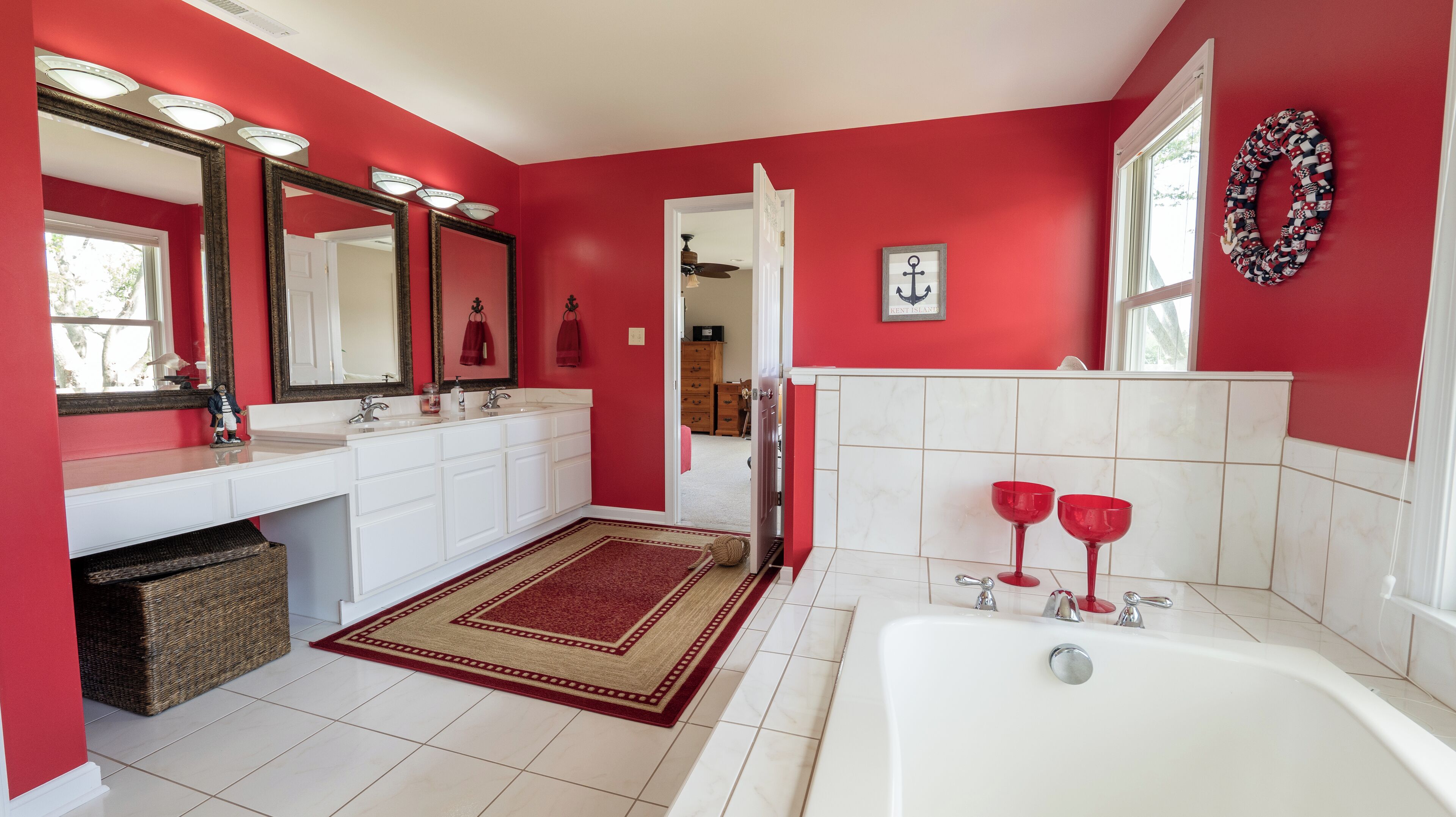 Ein Badezimmer mit roten Wänden, einem weißen Waschtisch, einem großen Spiegel und einer Badewanne.
