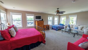 A bedroom with a bed, a desk, a dresser, a chair, a sofa, a TV, and a ceiling fan. - 4 Bedroom Waterview - MD Chesapeake Bay! Walk to Marina, Beach Bar & Restaurant! (Stevensville)