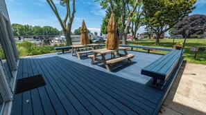 A covered outdoor deck with picnic tables and umbrellas, surrounded by trees and a parking area. - 4 Bedroom Waterview - MD Chesapeake Bay! Walk to Marina, Beach Bar & Restaurant! (Stevensville)