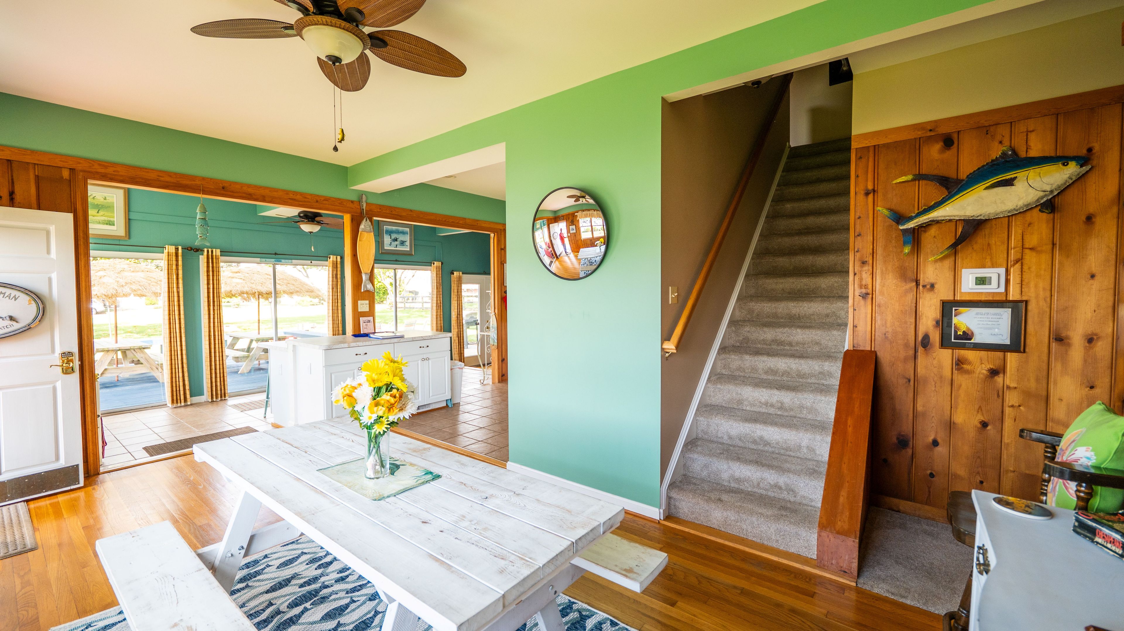 A room with a wooden staircase, a dining area with a white table, and a view of the outside.
