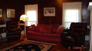 A cozy living room with a red patterned sofa, two leather armchairs, a floor lamp, and framed pictures on the walls. - Quiet, Private, 2 acres to enjoy and still close to everywhere you want to go. (Elkins)