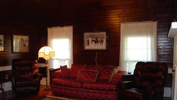 A cozy living room with a red patterned sofa, two leather armchairs, a floor lamp, and framed pictures on the walls.