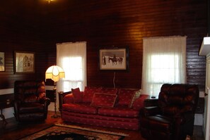 A cozy living room with a red patterned sofa, two leather armchairs, a floor lamp, and framed pictures on the walls. - Quiet, Private, 2 acres to enjoy and still close to everywhere you want to go. (Elkins)
