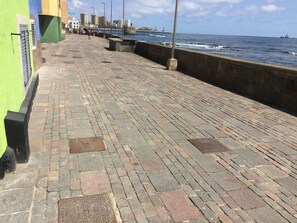 Ein gepflasterter Uferweg mit Steinbord und Blick auf das Meer.