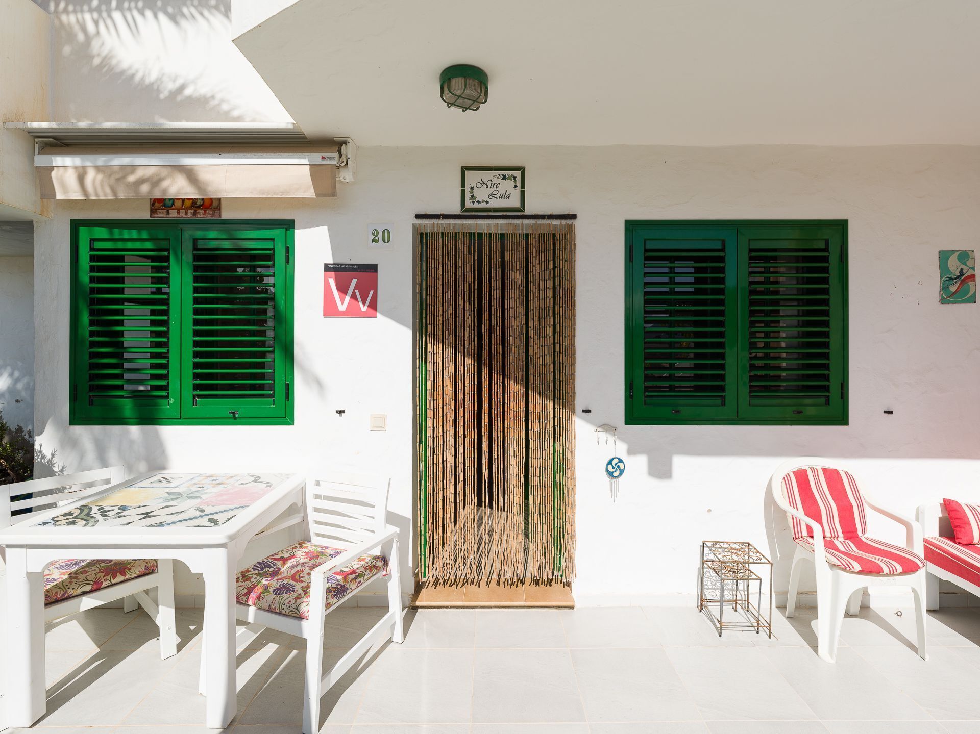 A white building with green shutters, a tiled patio, and a table with chairs.