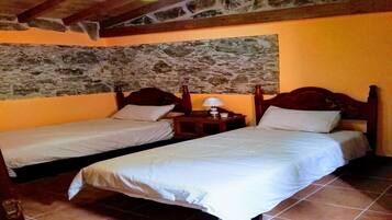 Una habitación con dos camas individuales, cabeceros de madera, pared de piedra y suelo de baldosas.
