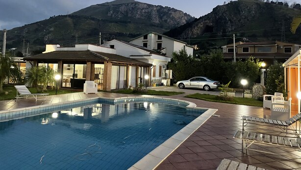 Ein Schwimmbad mit gefliestem Deck, einer Lounge-Bereich mit Stühlen und Blick auf Berge im Hintergrund.