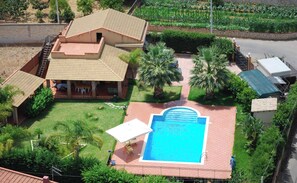 A residential property with a swimming pool, a covered patio, and a garden with palm trees.