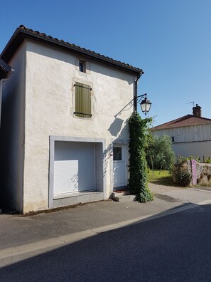 Een gebouw met twee verdiepingen, een witte gevel, een garagepoort en een klein raam met luiken.