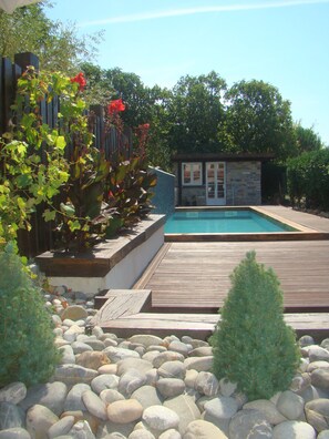Ein Schwimmbecken mit Holzterrasse, umgeben von Steinen und Pflanzen.