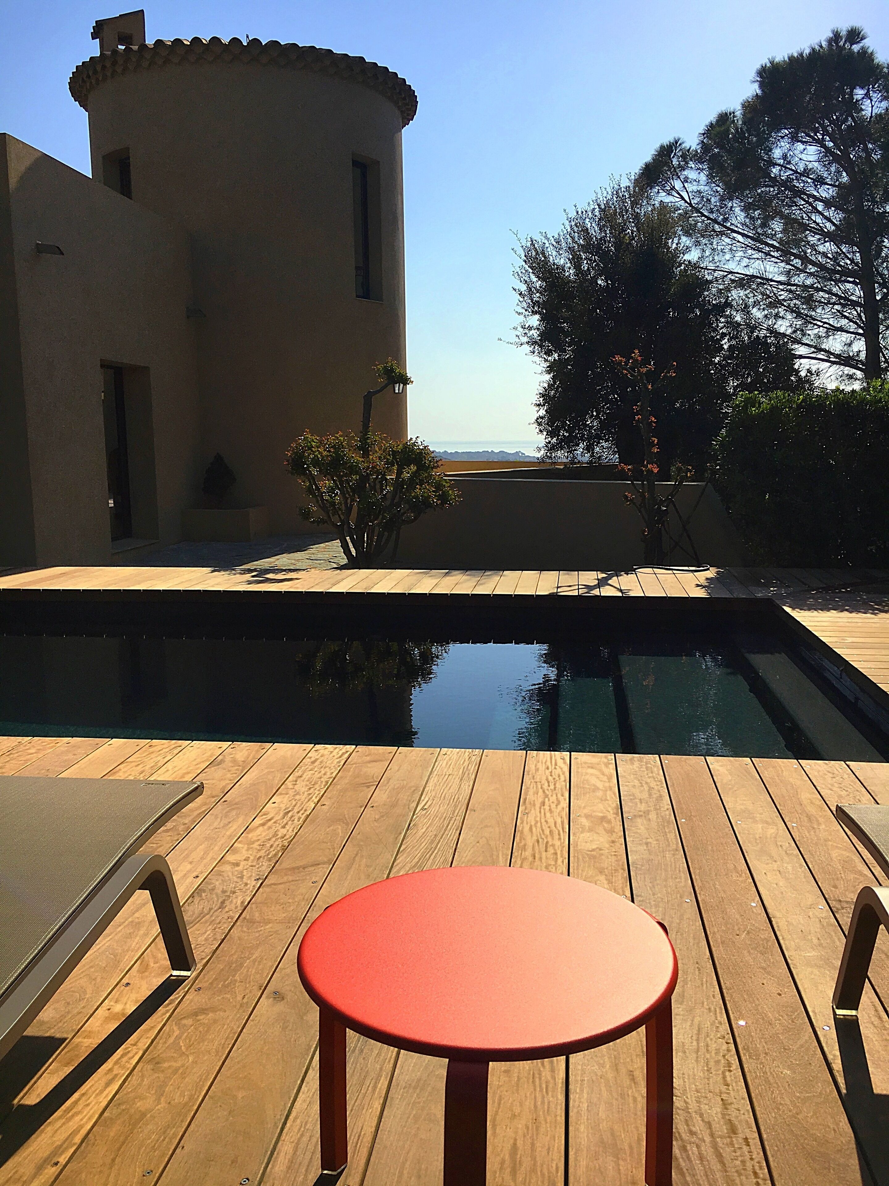 En træterrasse med rødt bord og stole, en swimmingpool og en bygning med udsigt over landskabet.