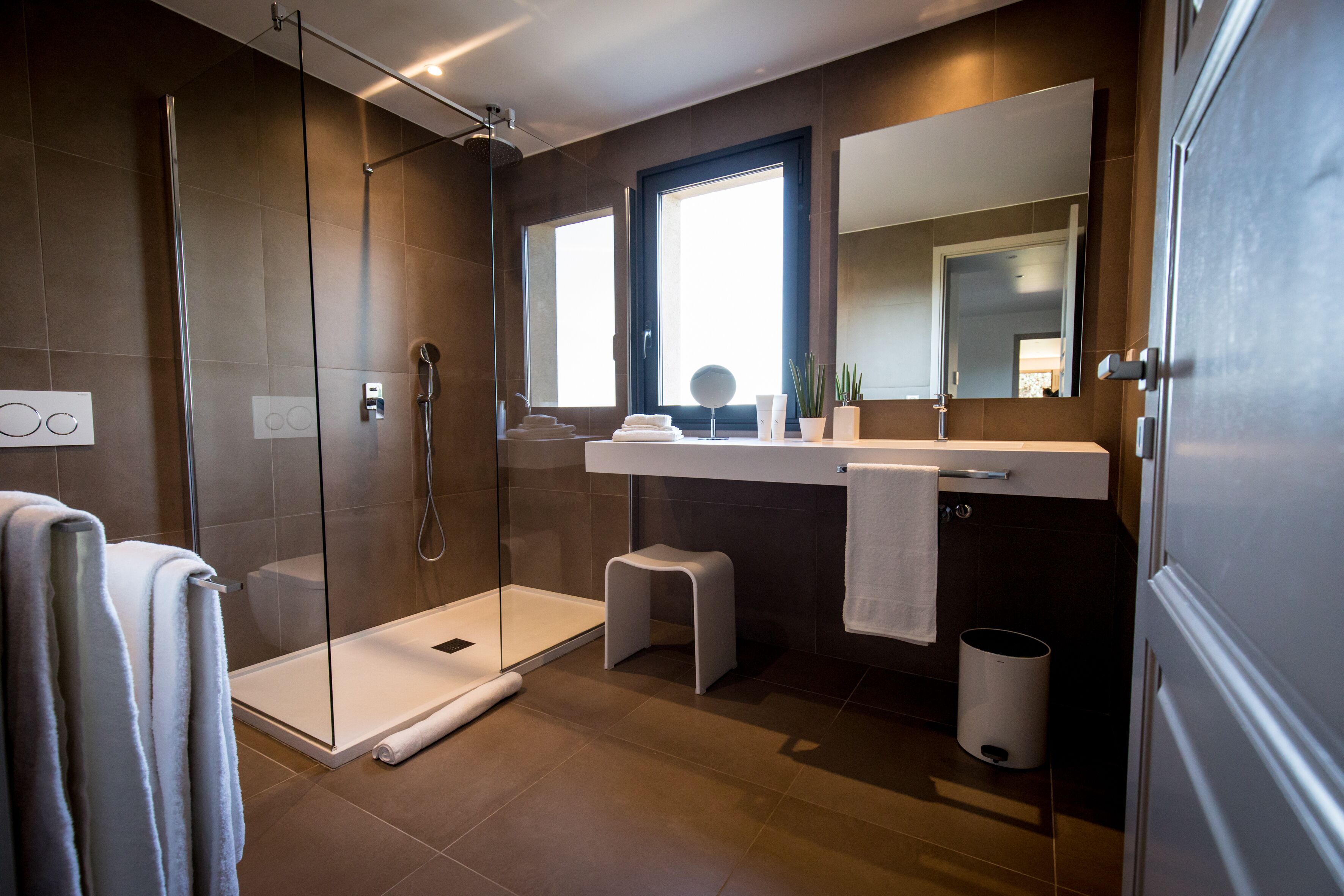 Une salle de bain moderne avec une douche à parois de verre, un meuble-lavabo avec un miroir et un petit tabouret.