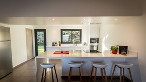 A modern kitchen with a central island, bar stools, a refrigerator, and a window with a view of greenery. - New: Villa 200 m2 with sea view and heated swimming pool, 4 bedrooms. (Porto-Vecchio)