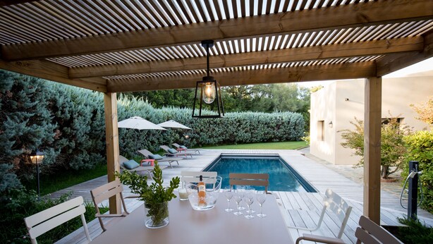 A covered outdoor dining area with a pool, wooden deck, and lounge chairs. - New: Villa 200 m2 with sea view and heated swimming pool, 4 bedrooms. (Porto-Vecchio)
