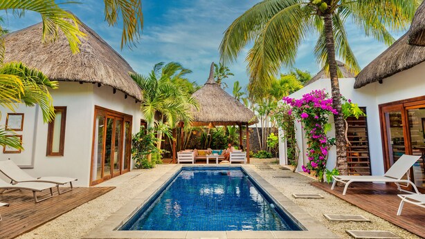 A pool area with thatched-roof structures, lounge chairs, and a small seating area.