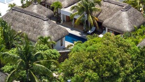 A resort with thatched-roof villas, a swimming pool, and lush tropical vegetation.
