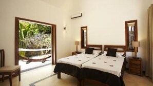 A double bed with a white and black bedspread, two bedside tables with lamps, a wooden chair, and a large window with a view of greenery.