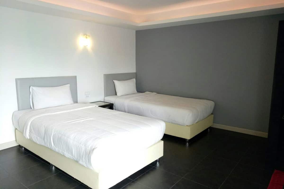 A hotel room with two beds, a nightstand, a wall-mounted light, and a dark tiled floor.