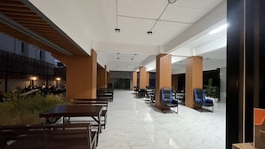 Amplio espacio interior con un largo pasillo, bancos de madera y zonas de estar con sillas.