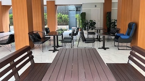 Un patio al aire libre con pilares de madera, sillas negras y azules, y piso de baldosas de mármol.
