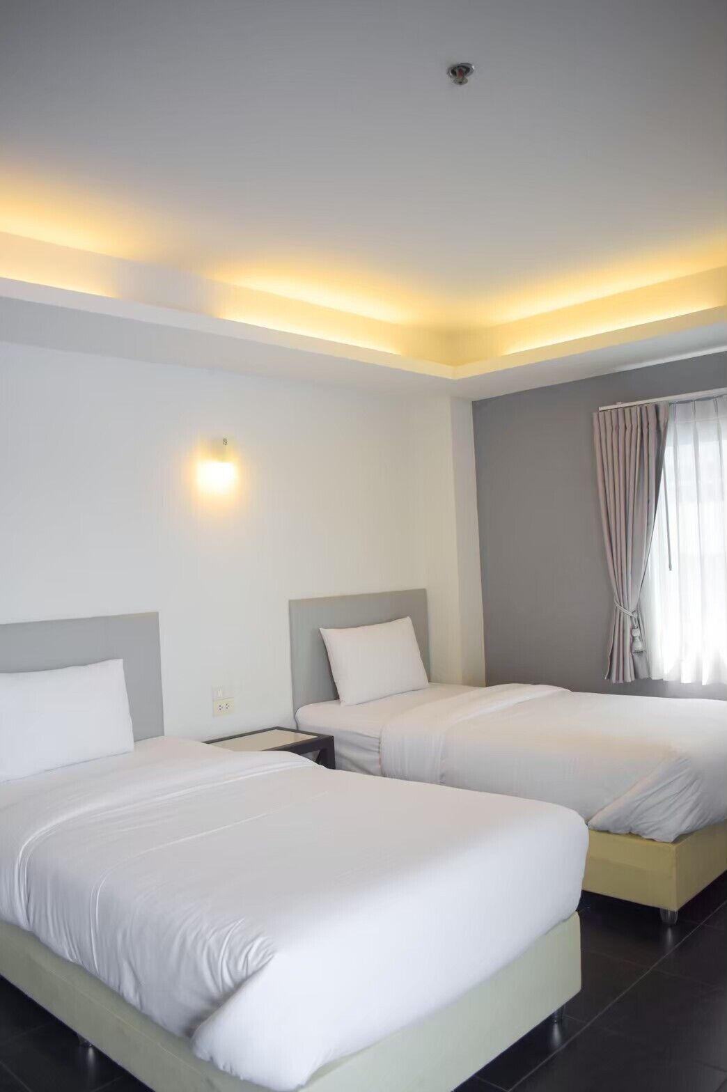 A hotel room with two beds, a ceiling light, and a window with curtains.