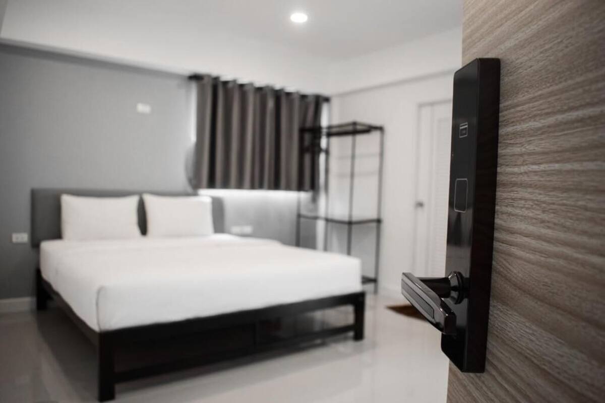 A modern bedroom with a bed, a wardrobe, and a wall-mounted control panel.