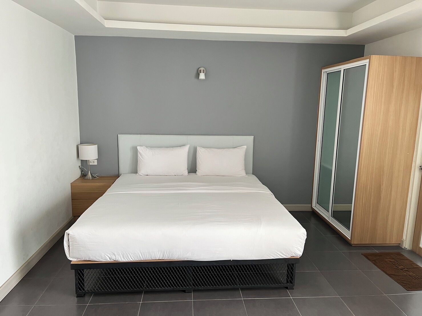 A modern bedroom with a large bed, a nightstand, a wardrobe, and a ceiling light.