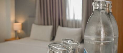 Una habitación de hotel con una cama, una mesita de noche, una lámpara y una mesa con una botella y vasos.