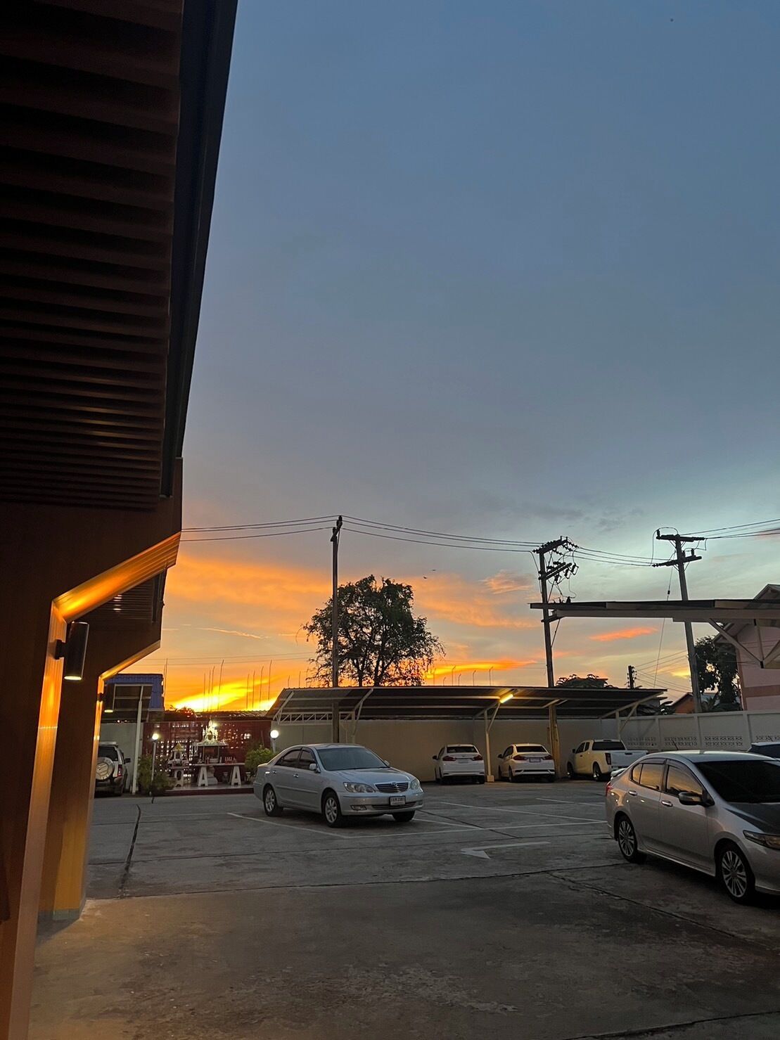 A parking lot with several cars, a building with a sloped roof, and a sunset in the background.