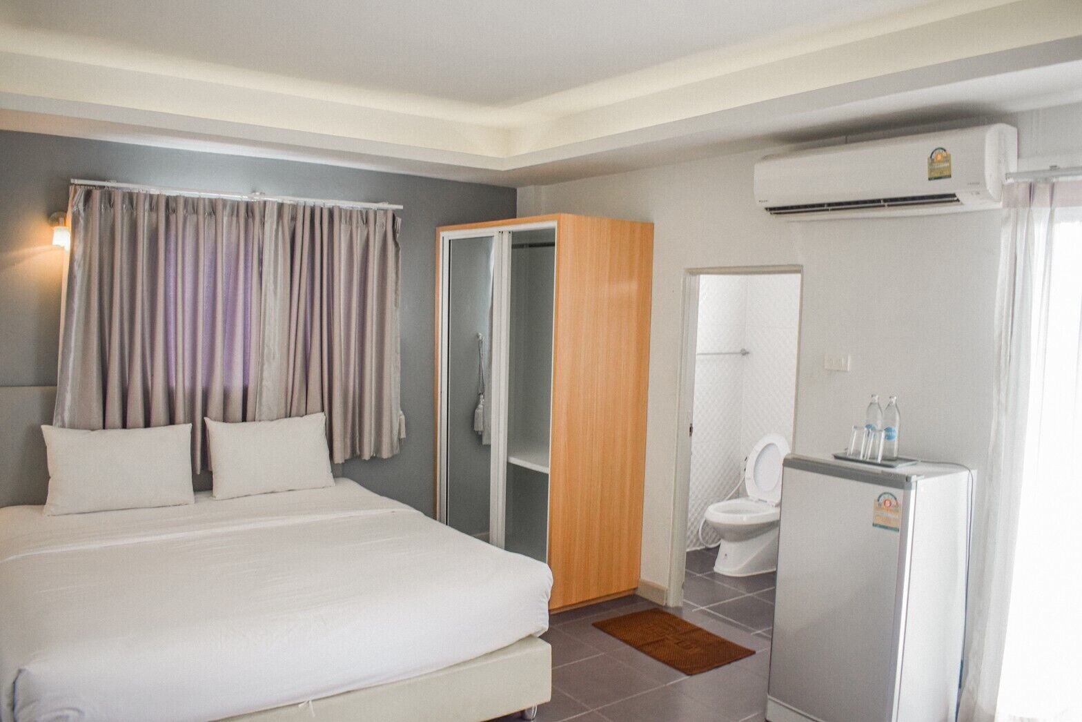 A hotel room with a bed, a wardrobe, a bathroom with a toilet and sink, and an air conditioning unit.