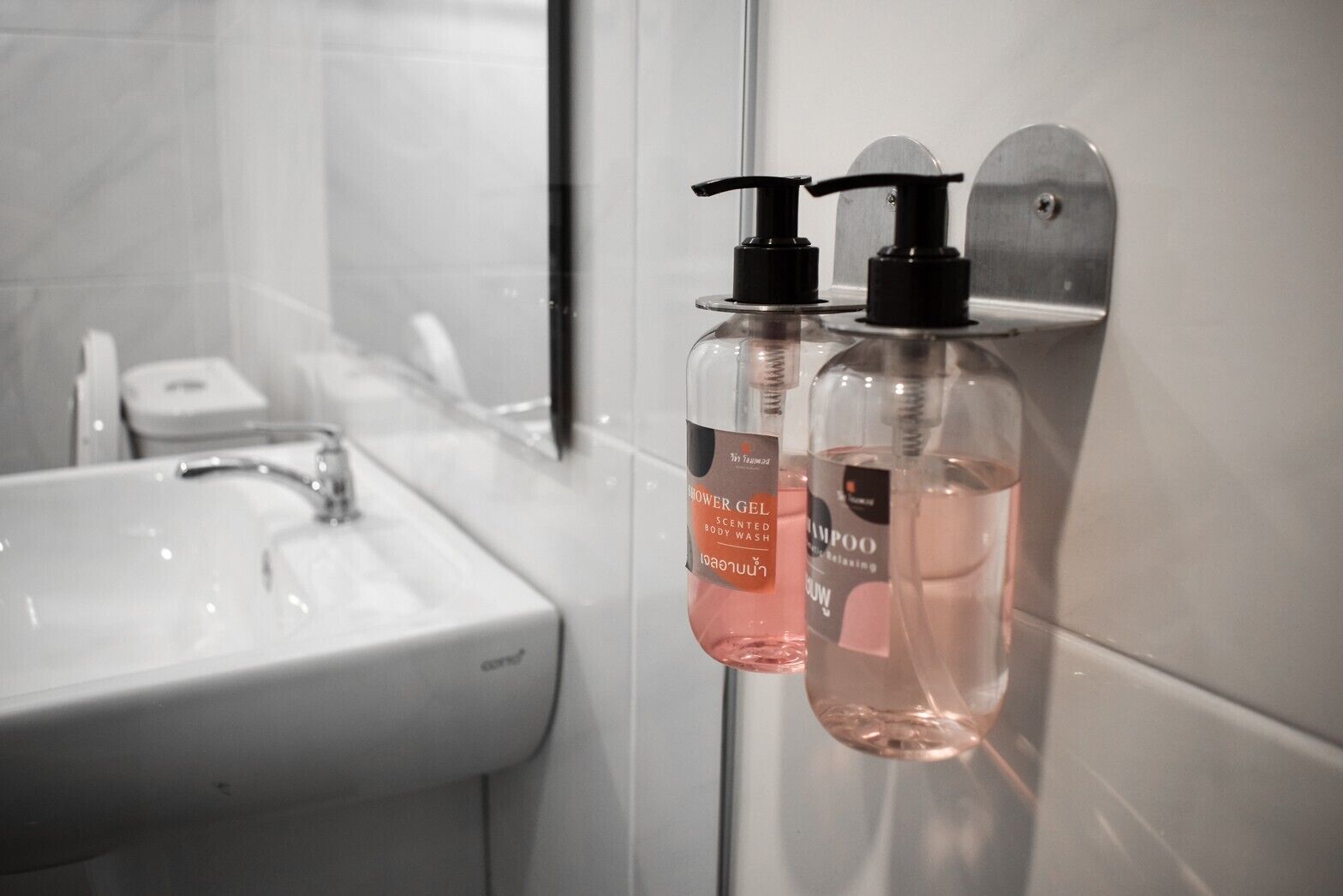 Un baño con un lavamanos blanco, dos botellas de gel de ducha y champú, y un espejo.